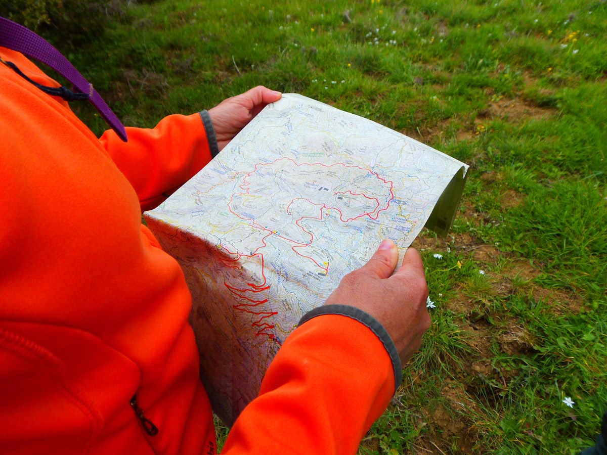 Laptop displaying topographic maps and satellite imagery of mountain elk habitat next to binoculars and a hunting journal on a wooden desk